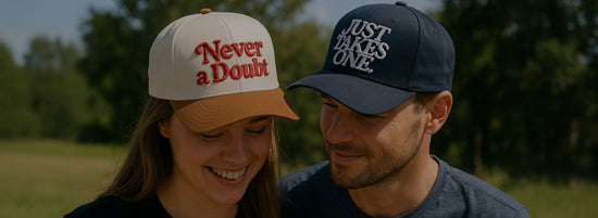 A smiling couple wearing baseball caps outdoors — the woman’s cap reads “Never a Doubt,” and the man’s cap says “Just Takes One.”